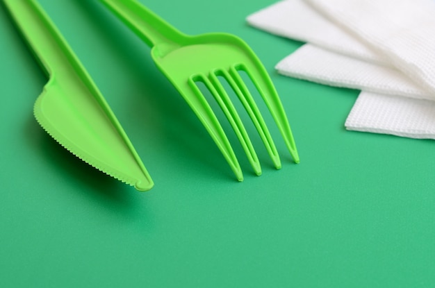 Couverts en plastique jetables verts. Fourchette et couteau en plastique reposent sur une surface de fond verte à côté de serviettes