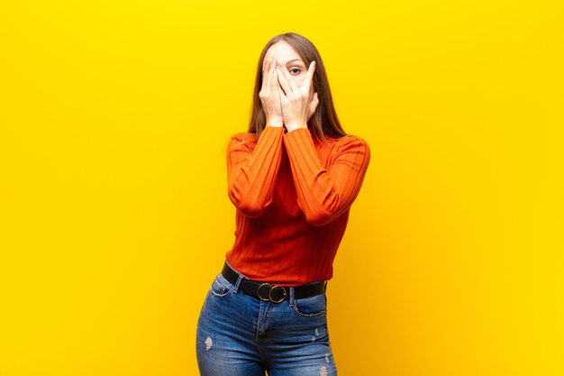 couvrant le visage avec les mains, jetant un coup d'œil entre les doigts avec une expression surprise et regardant sur le côté