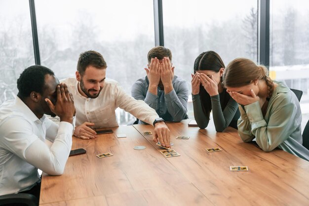 Couvrant les yeux avec les mains Jouant au jeu de cartes Une équipe d'employés de bureau est ensemble à l'intérieur