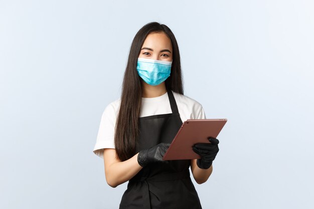 Covid-19, distanciation sociale, petite entreprise de café et concept de prévention des virus. Sourire mignon barista asiatique, personnel féminin du café prenant la commande avec tablette numérique, porte un masque médical et des gants