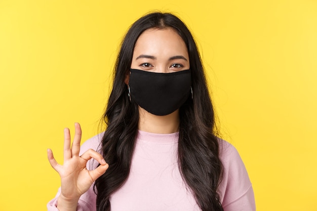 Photo covid-19, mode de vie de distanciation sociale, empêche le concept de propagation du virus. gros plan d'une femme asiatique souriante et heureuse en masque facial, prenez tout sous contrôle, montrez une bonne connexion, aimez et recommandez.