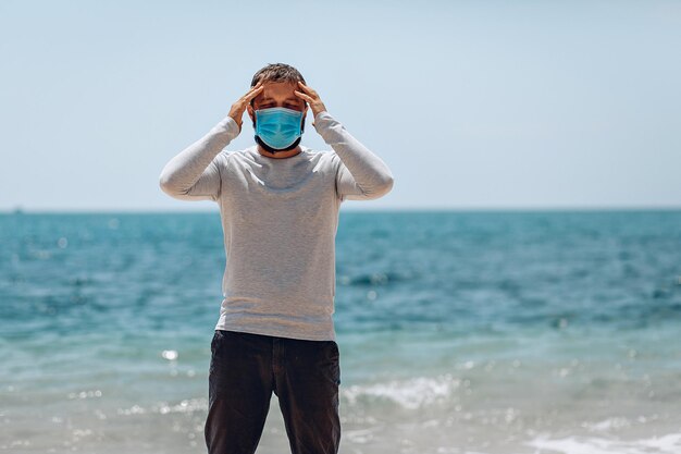 COVID-19 Pandemic Coronavirus homme sur la plage portant un masque protecteur pour la propagation de la maladie du coronavirus 2020 et touchant son front. Notion de SRAS-CoV-2