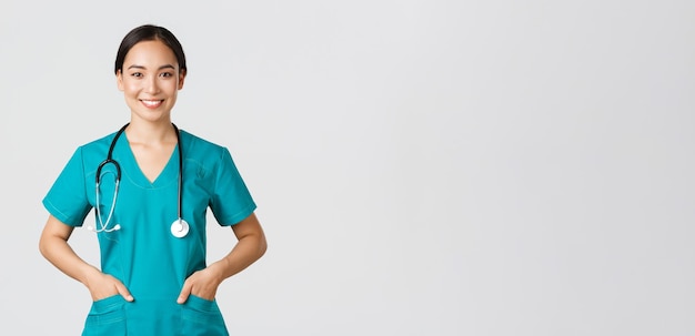 Covid-19, travailleurs de la santé, concept de pandémie. Une jolie femme médecin asiatique souriante et confiante, un médecin qui a l'air déterminé et optimiste, se tenant la main dans des poches de gommages, examine les patients en clinique.