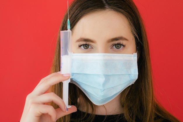 COVID19 Pandémie Coronavirus Jeune fille sur fond rouge masque protecteur tenant une seringue C
