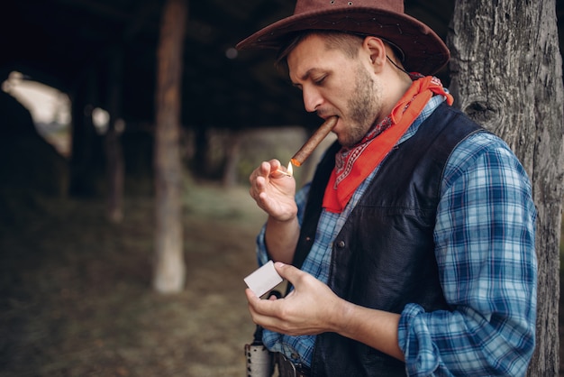 Cowboy brutal allume un cigare avec des allumettes, Texas Ranch, Western. Vintage personne de sexe masculin se détendre à la ferme, mode de vie du Far west