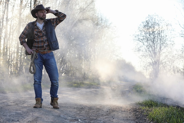 Un Cowboy Dans Un Chapeau Et Un Gilet Se Tient Dans Une épaisse Fumée Sur La Route