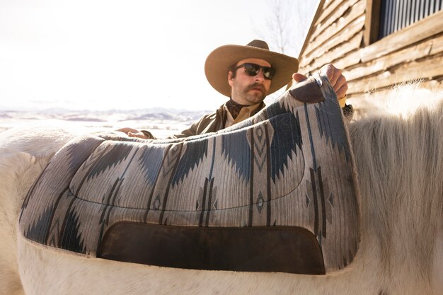 Photo cowboy mettant la selle sur le cheval