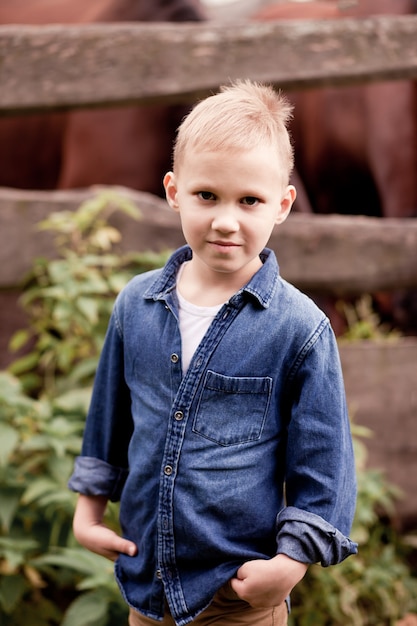 Cowboy mignon d'enfant se tenant près d'une clôture en bois avec des chevaux