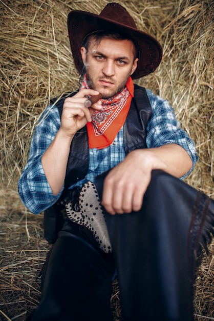 Photo cowboy se détendre avec un cigare, une botte de foin