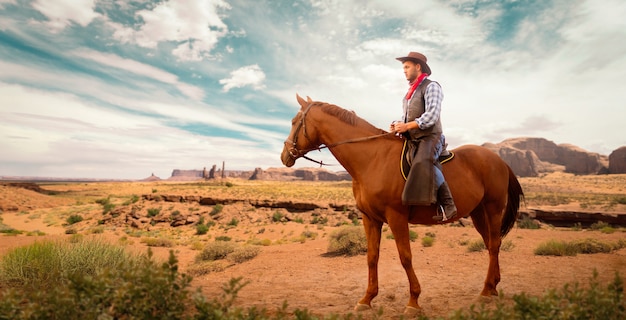 Cowboy en vêtements de cuir à cheval dans la vallée du désert, dans l'ouest. Cavalier vintage à cheval, aventure de l'ouest sauvage