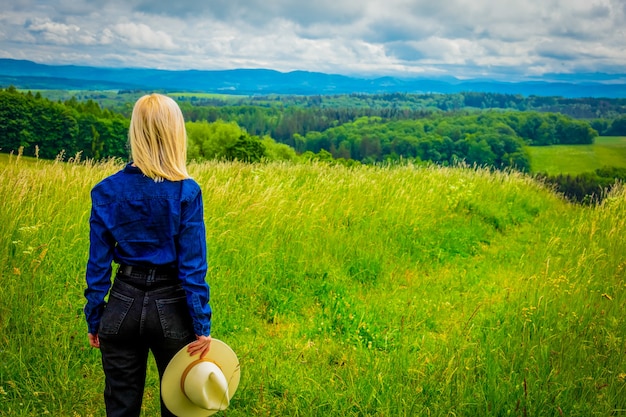 Cowgirl blonde au chapeau au pré avec des montagnes derrière