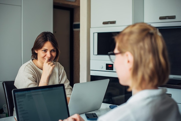 Coworking, télétravail, télétravail, startup. Deux jolies jeunes femmes assises avec des ordinateurs portables face à face, se concentrent sur le visage de la brune.