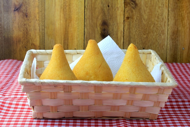 Coxinha dans le panier, collations de la cuisine brésilienne traditionnelle farcie au poulet, isolé sur une table en bois rustique