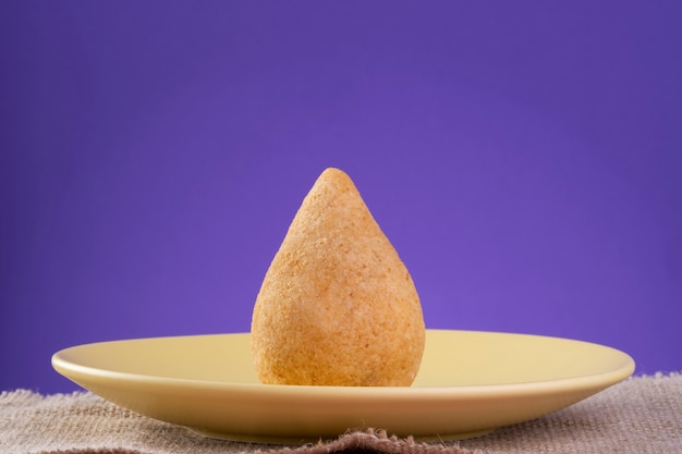 Coxinha frit sur une plaque jaune avec un fond violet.