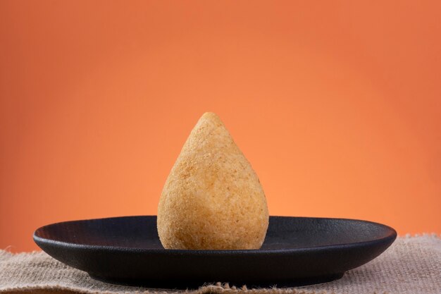 Coxinha frit sur une plaque noire avec un fond orange.