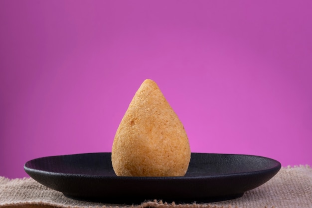 Coxinha sur plaque noire avec fond rose.