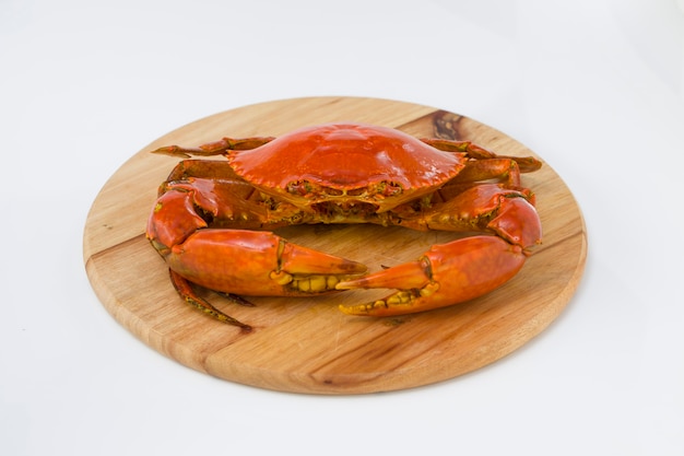 Crabe de boue cuit, disposé sur une base en bois avec fond texturé blanc, vue de dessus.