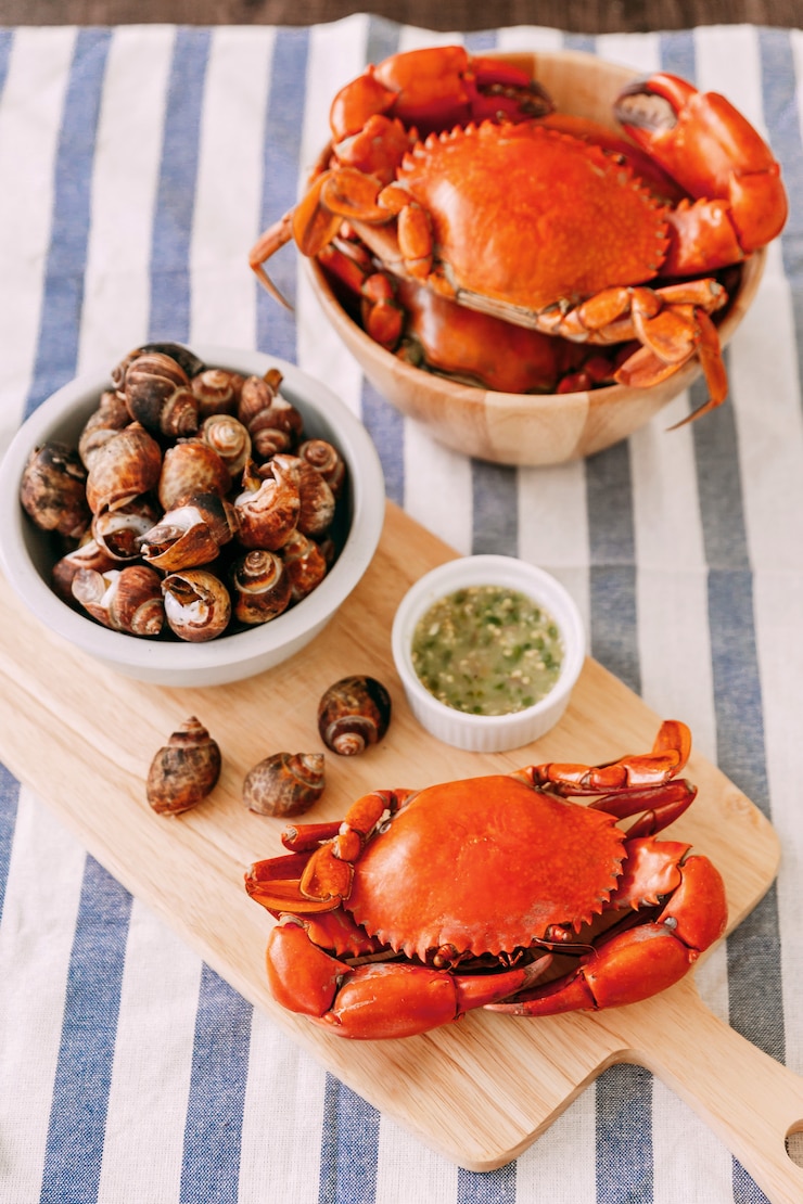 Photo crabe de boue géant cuit à la vapeur sur une planche à découper en bois servi avec une sauce aux fruits de mer épicée thaïlandaise et un canevas laevistrombus grillé dans une coquille.