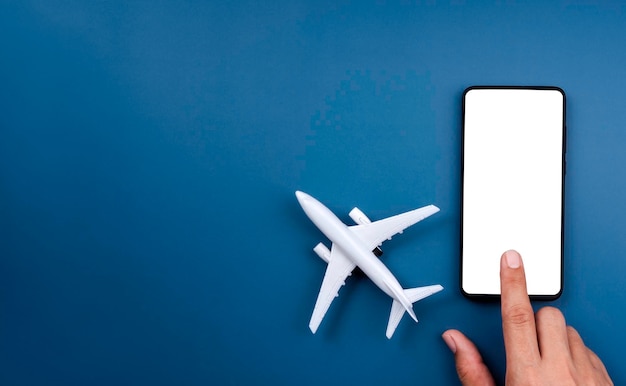Écran blanc vide sur smartphone avec doigt touchant et jouet modèle d'avion sur fond bleu avec espace de copie. Réservation de billets d'avion sur l'application de téléphonie mobile, les voyages en ligne et les concepts d'assurance vacances.