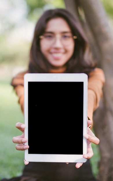 Écran de tablette vierge montrant une femme heureuse sur fond de parc. Focus sur la tablette.