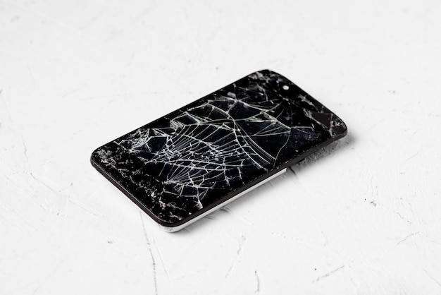 Écran de téléphone cassé sur fond blanc De nombreuses fissures sur l'écran tactile noir du téléphone