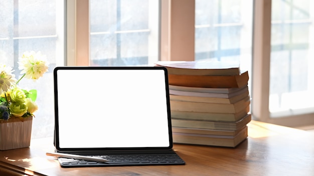 Écran vide de tablette numérique et livres sur table en bois.