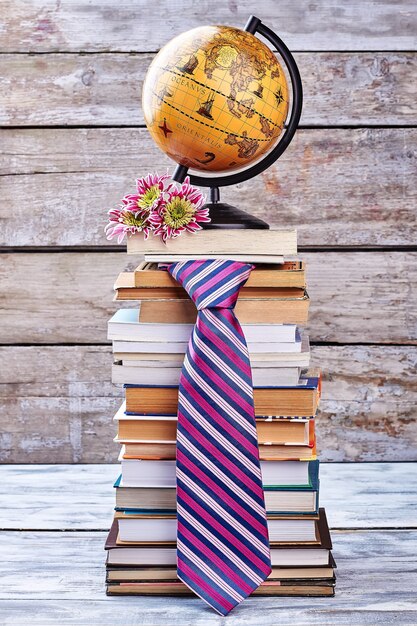 Cravate, fleurs et globe. Pile de livres sur étagère.