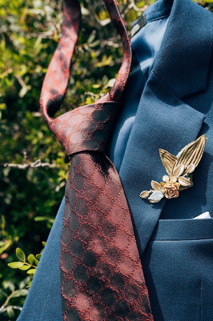 Une cravate rouge foncé et une veste bleue avec une boutonnière sur des feuilles vertes