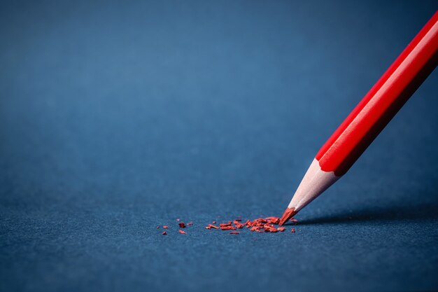 Crayon pointu rouge avec des morceaux de graphite sur une feuille de papier texturé bleu. Le concept de créativité d'idée, d'éducation, d'entreprise.