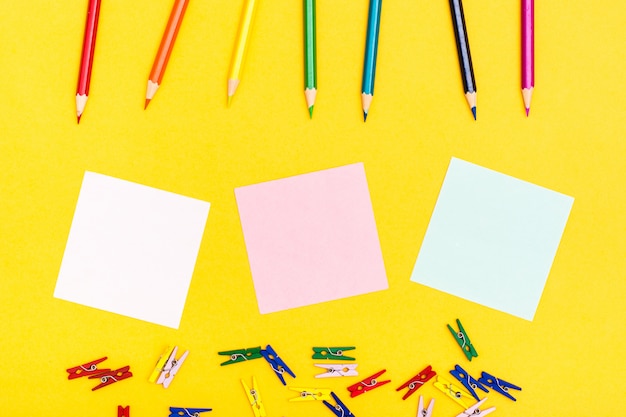 Crayons en bois colorés, épingles et feuilles pour écrire sur un fond jaune