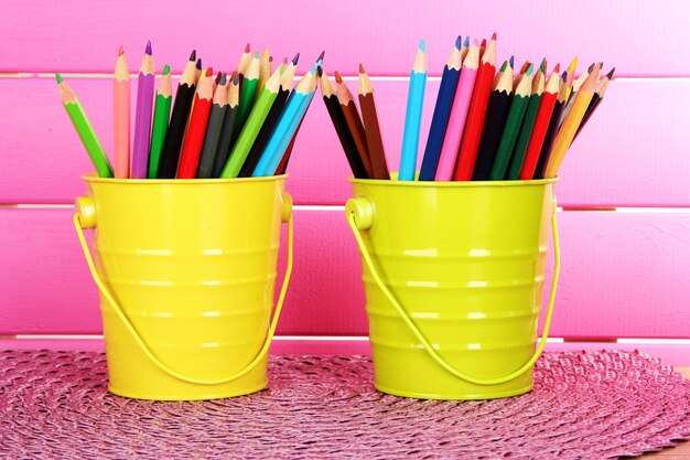 Photo crayons colorés dans deux seaux sur table sur fond rose