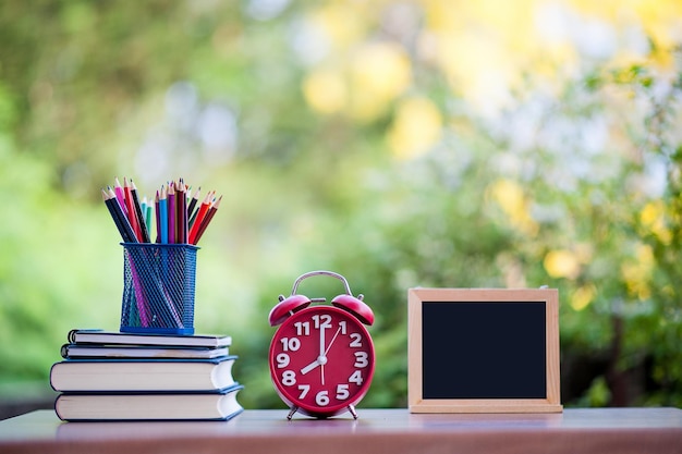 Photo des crayons colorés avec des livres et un réveil sur la table.