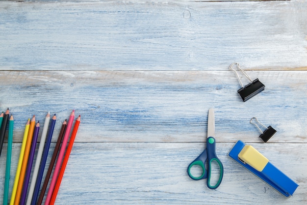 crayons de couleur ou crayons de couleur, ciseaux, agrafeuse sur bois vintage éraflé bleu et blanc, vue de dessus