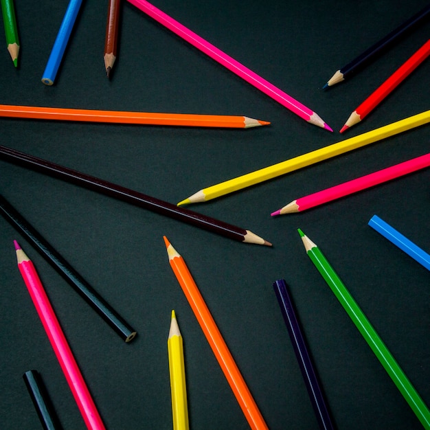 Crayons de couleur dispersés dans tout le cadre sur fond noir. Mise à plat, vue de dessus