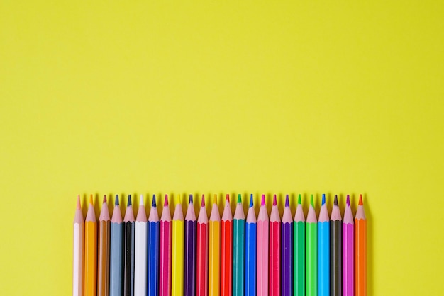 Crayons de couleur sur fond jaune vue de dessus retour au concept d'école