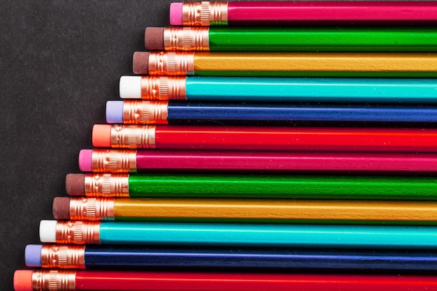 Crayons de différentes couleurs d'affilée sur un fond texturé noir.