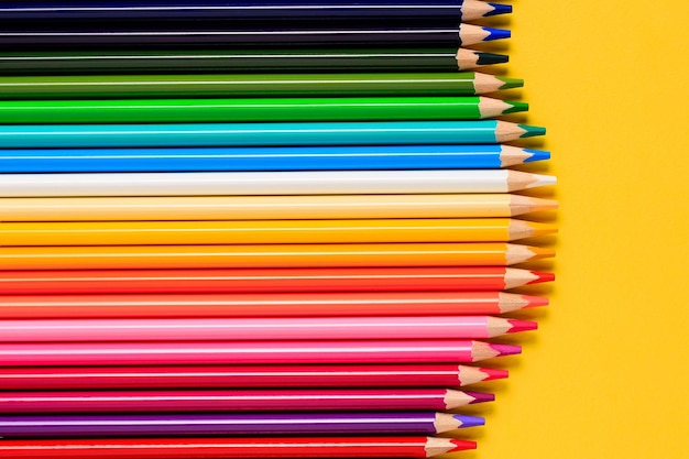 Crayons multicolores sur fond jaune Crayons de couleur mis en rangée des crayons de couleur en bois pour le dessin