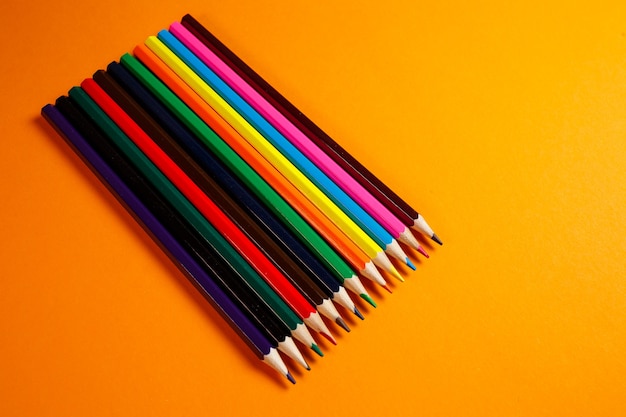 Crayons multicolores pour le dessin empilés sur fond orange. Articles de papeterie