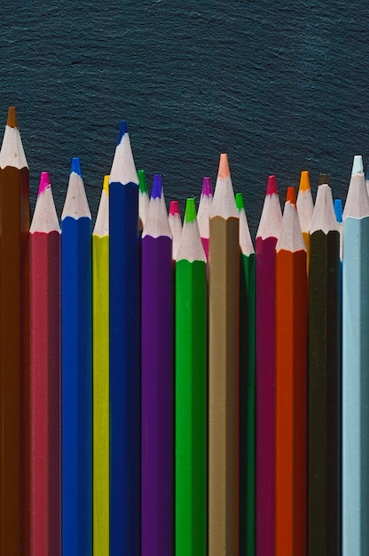 Les Crayons Multicolores Se Trouvent Sur Un Fond Texturé Noir.