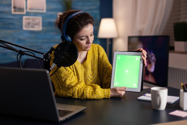 Créateur de médias sociaux avec casque de production tenant une maquette de tablette à clé chroma à écran vert avec affichage isolé enregistrant un podcast en ligne à l'aide d'un équipement de diffusion en direct. Vlogger diffuse du contenu en direct