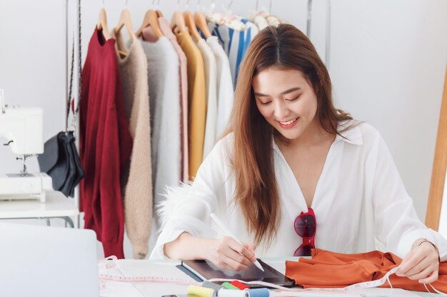 Créateur de mode de belle femme asiatique assis dans le magasin de vêtements et le studio. Devant l'ordinateur portable pour se réunir en ligne. Influenceur en ligne d'affaires sur le concept de médias sociaux.