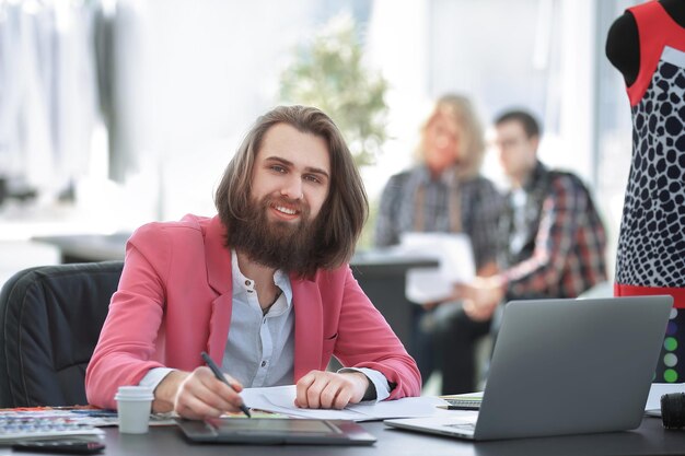 Créateur de mode souriant à la table dans un studio moderne