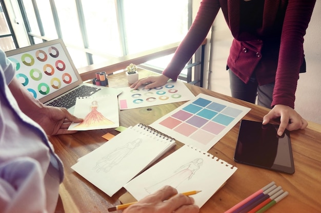 Des créateurs de mode dessinant sur un livre à leur bureau.