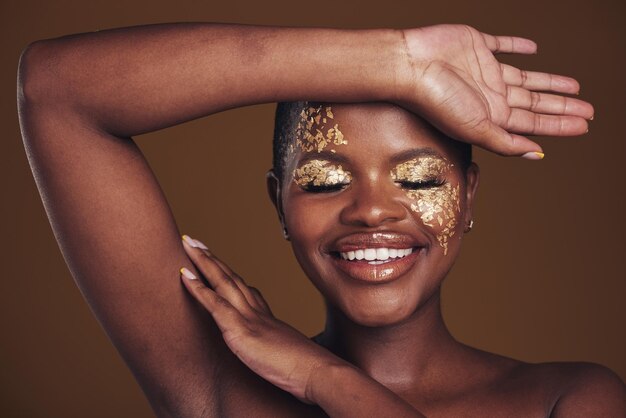 Créatif doré et art sur femme noire avec maquillage pour l'esthétique de la beauté isolée en studio fond marron yeux fermés Sourire luxe et visage de personne avec glamour cosmétique ou design pour les soins de la peau