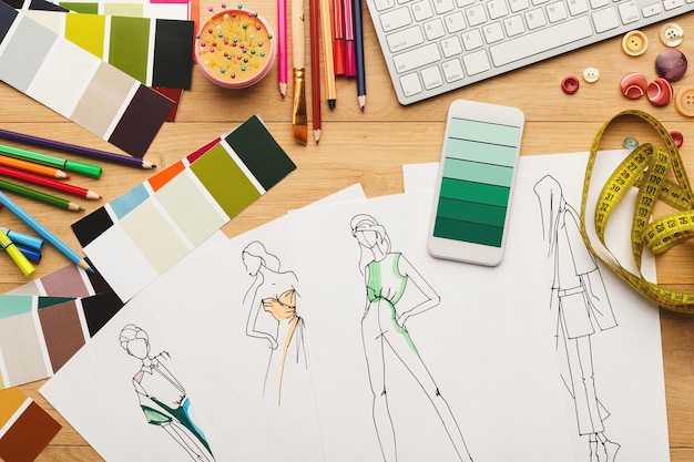 Photo création d'un nouveau fond de collection de mode. croquis dessinés à la main, smartphone avec des échantillons de couleurs à l'écran et accessoires design sur table en bois, vue de dessus. concept de créativité et de couture