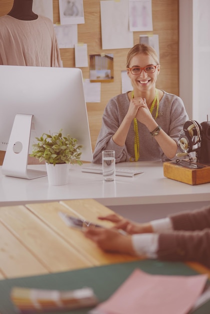 Création de nouveaux styles à la mode Jeune femme joyeuse cousant assise sur son lieu de travail dans un atelier de mode