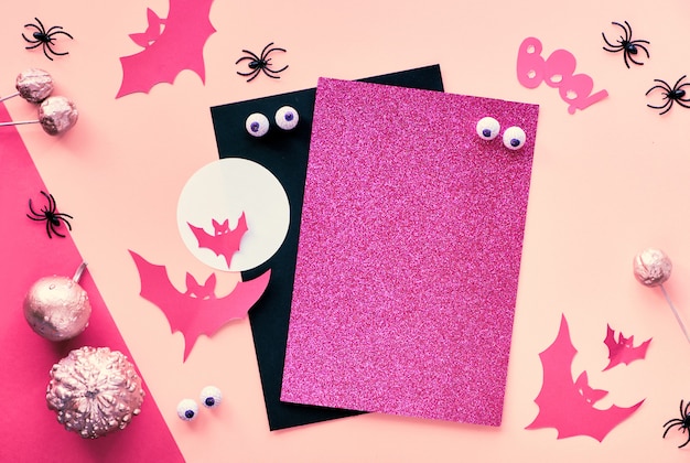 Créations en papier créatives Halloween à plat en rose, magenta et noir. Vue de dessus avec espace de cipy sur une pile de cartes, chauves-souris, yeux en chocolat, citrouilles et texte "Boo" sur papier divisé.