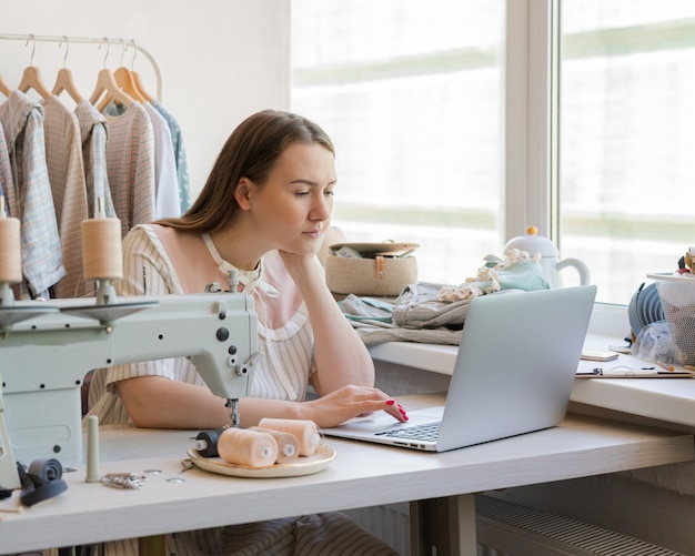 Créatrice de mode féminine créant des vêtements en ligne alors qu'elle était assise sur le lieu de travail avec la couture