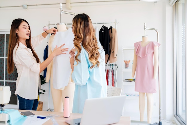 Créatrice de mode ou tailleur asiatique avec aide à la préparation d'un motif de tissu en papier découpé Couturière travaillant et concevant de nouvelles collections de mode pour les clients dans l'atelier de tailleur