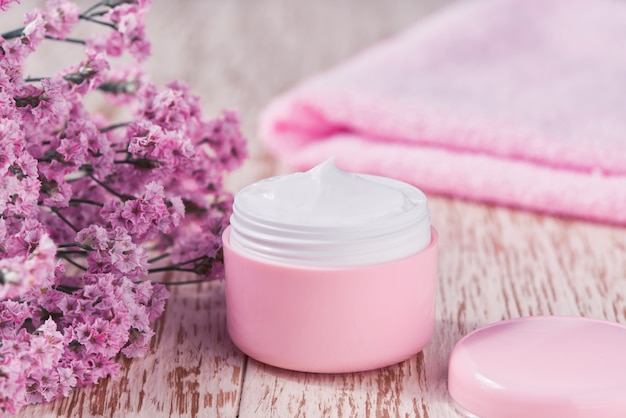 Crème anti-rides anti-âge soins du corps ou lotion hydratante pour l'hygiène du visage avec des fleurs roses dans un pot en plastique avec une serviette sur une table en bois.